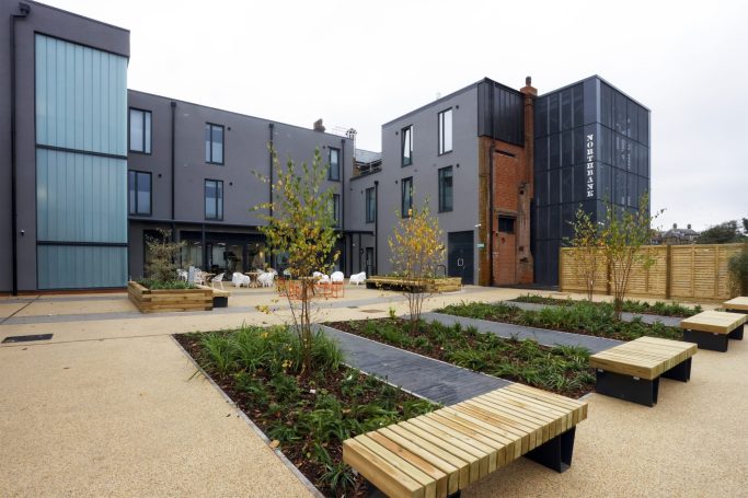 Rochester Independent College Modern building with landscaped gardens, wooden benches, and decorative trees.